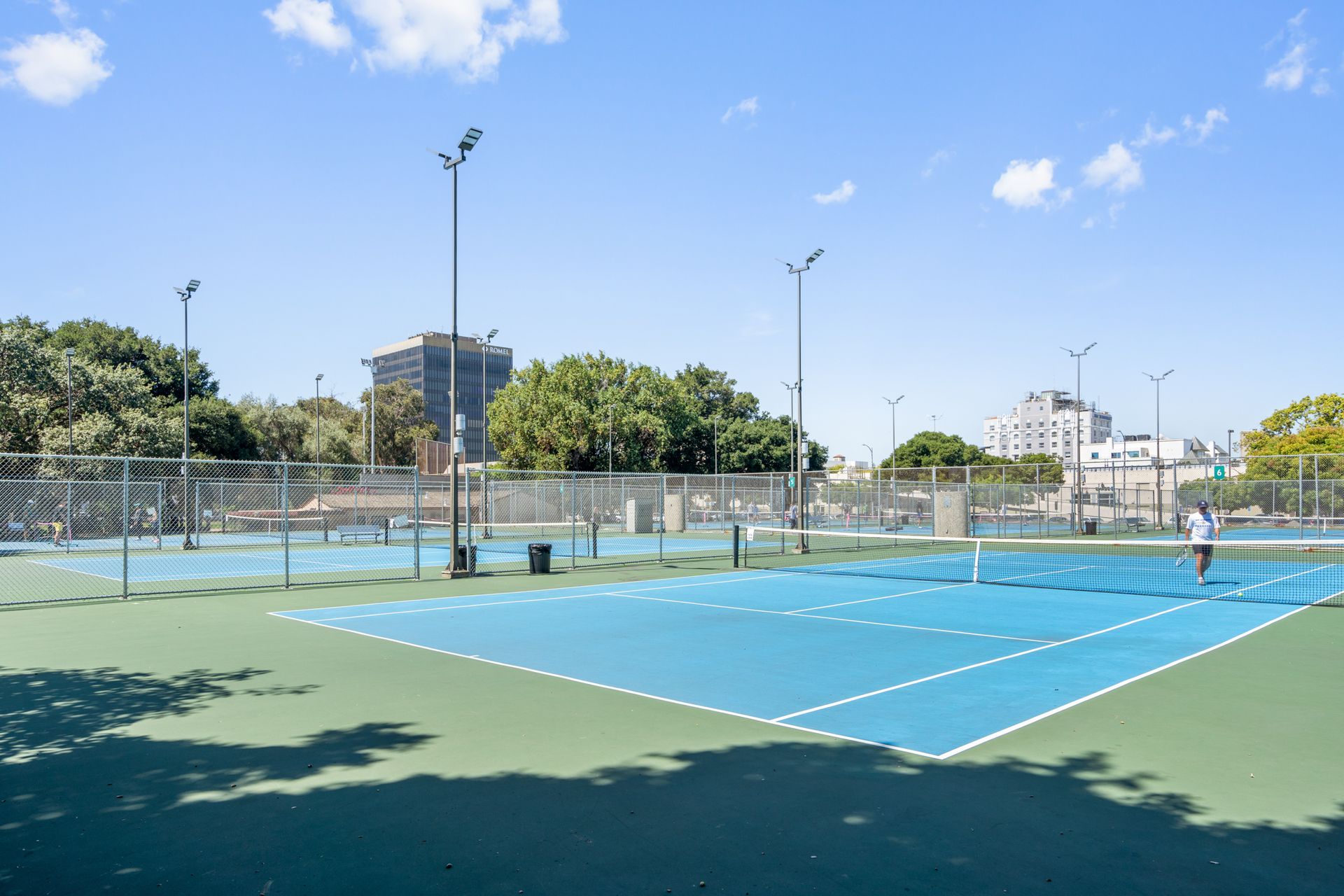 A man is playing tennis on a tennis court in a park.
