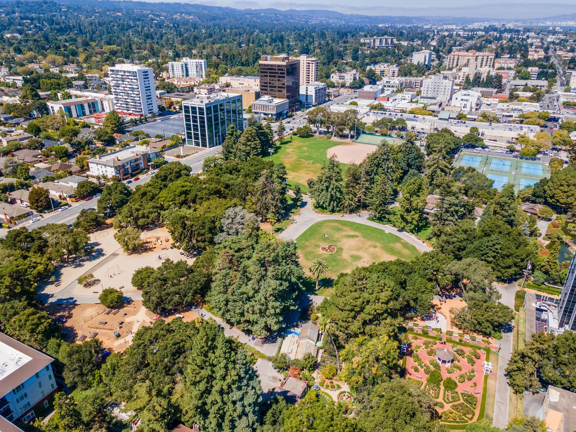 An aerial view of a park surrounded by trees and buildings in a city.