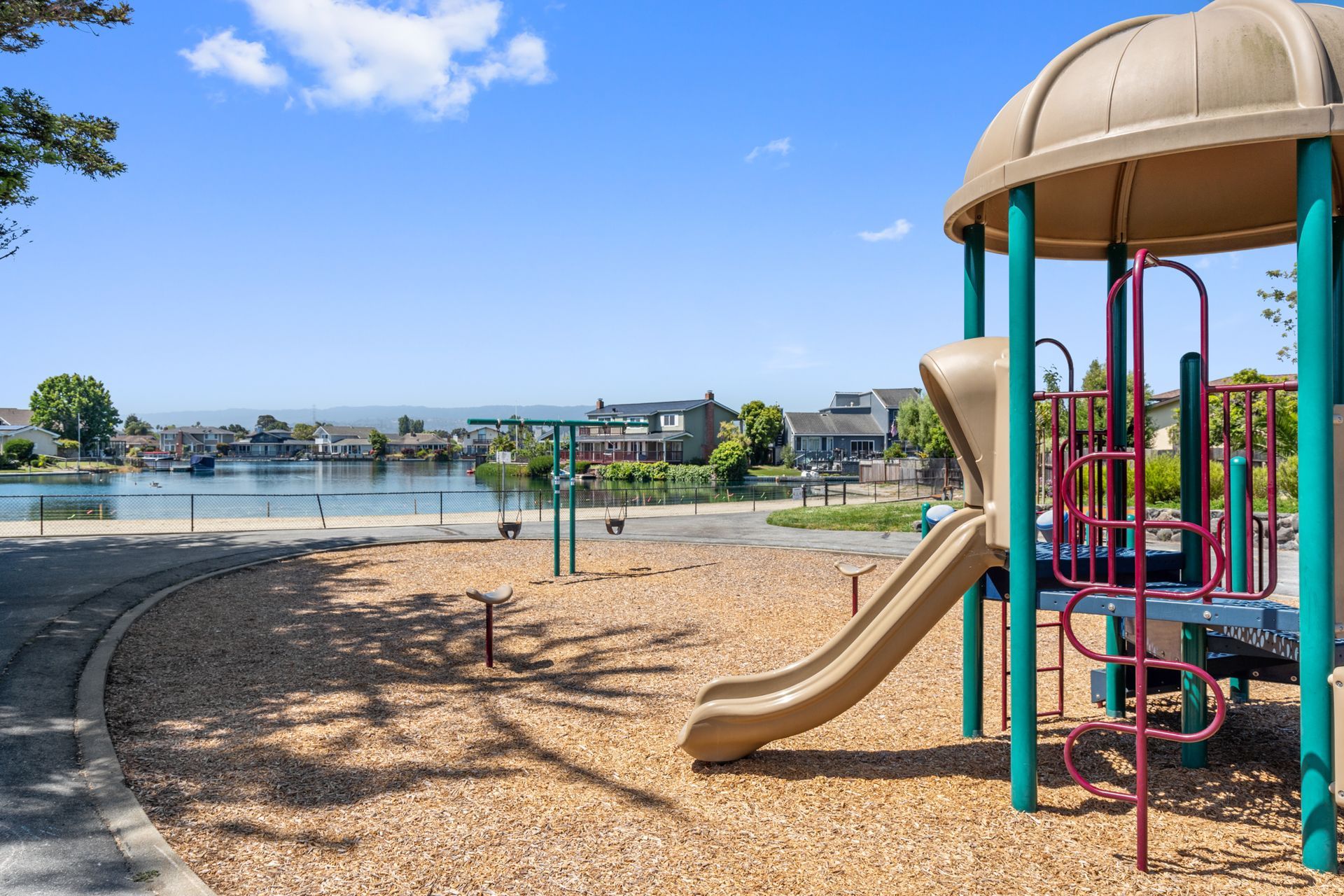 A playground with a slide and a canopy in a park with a lake in the background.