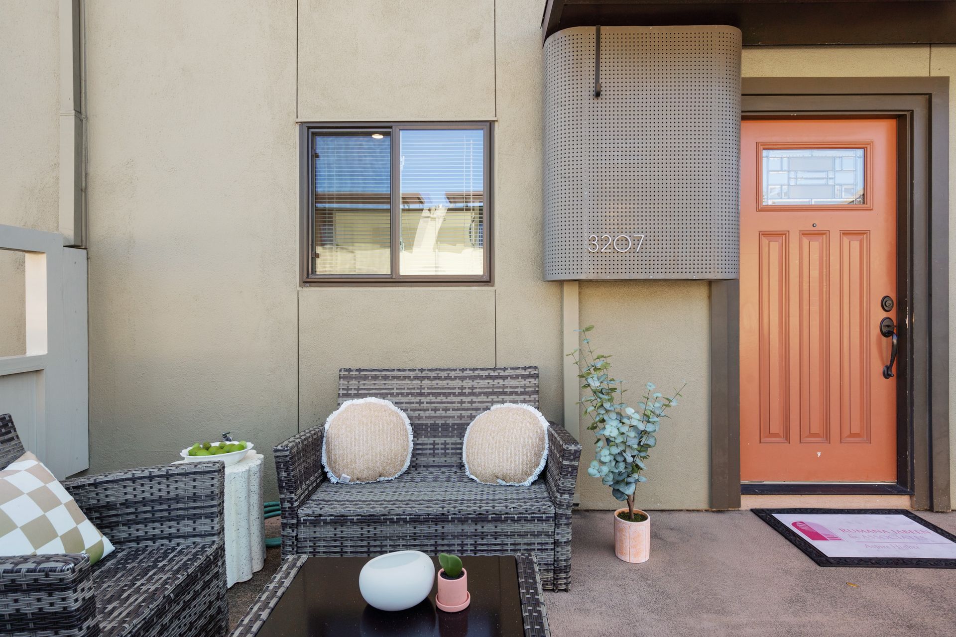 A patio with a couch , chairs and a table in front of a house with an orange door.