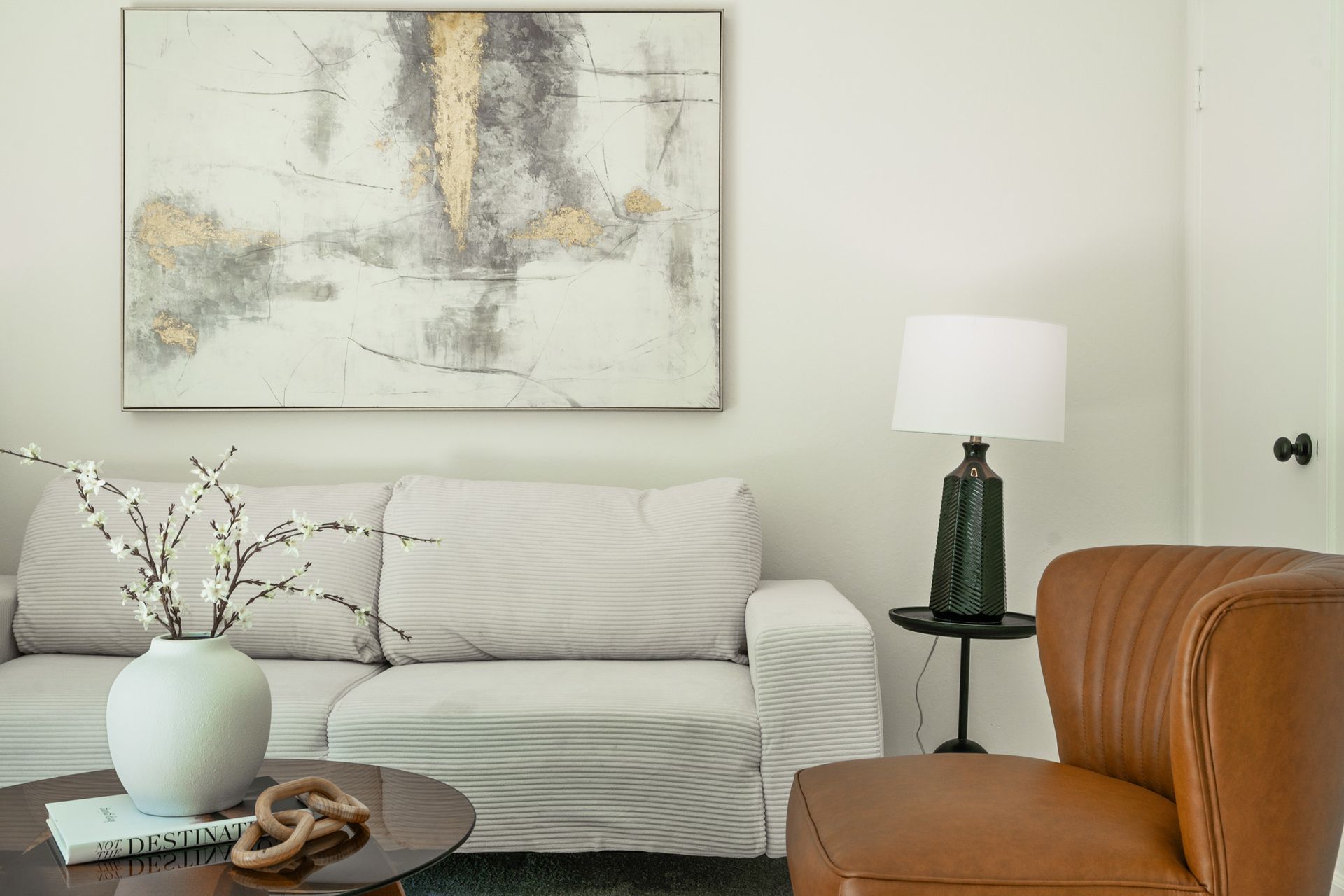 A living room with a couch , chair , table , lamp and painting on the wall.