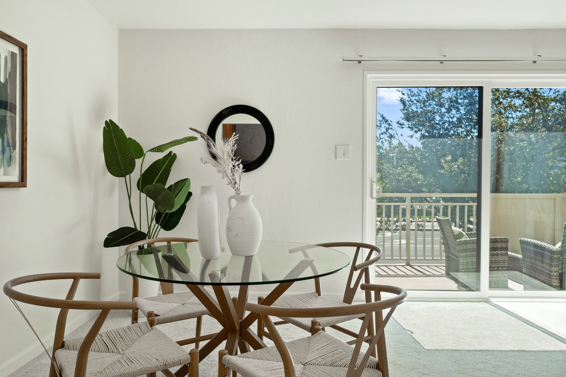 A dining room with a glass table and chairs and a sliding glass door leading to a balcony.
