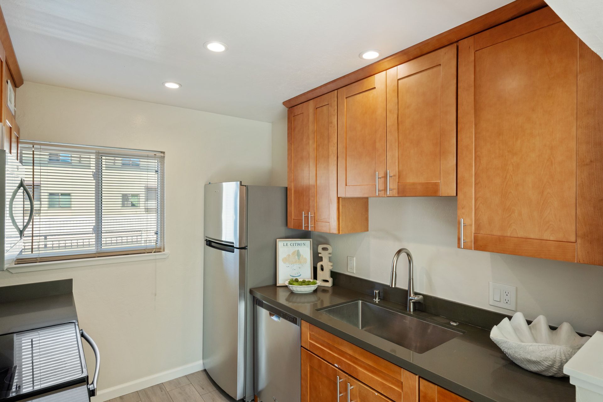 A kitchen with wooden cabinets , a stainless steel refrigerator , a sink , and a window.