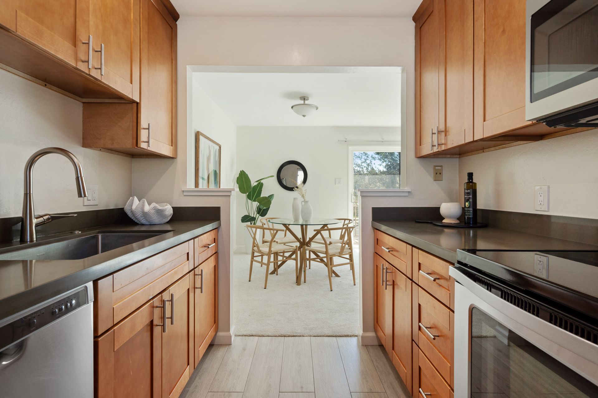 A kitchen with wooden cabinets and stainless steel appliances and a dining room in the background.