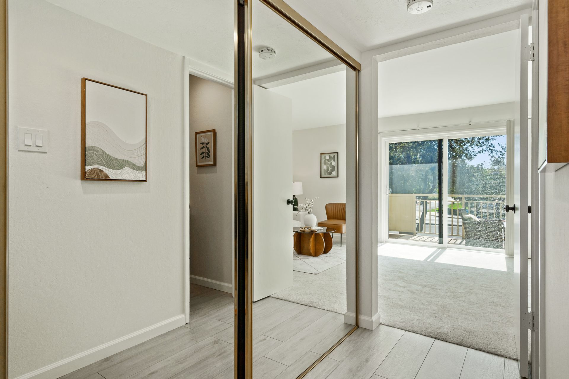 A hallway with a large mirror on the wall leading to a living room.
