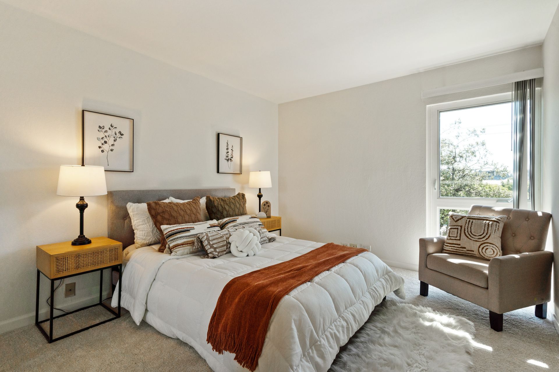A bedroom with a bed , chair , nightstand and lamps.