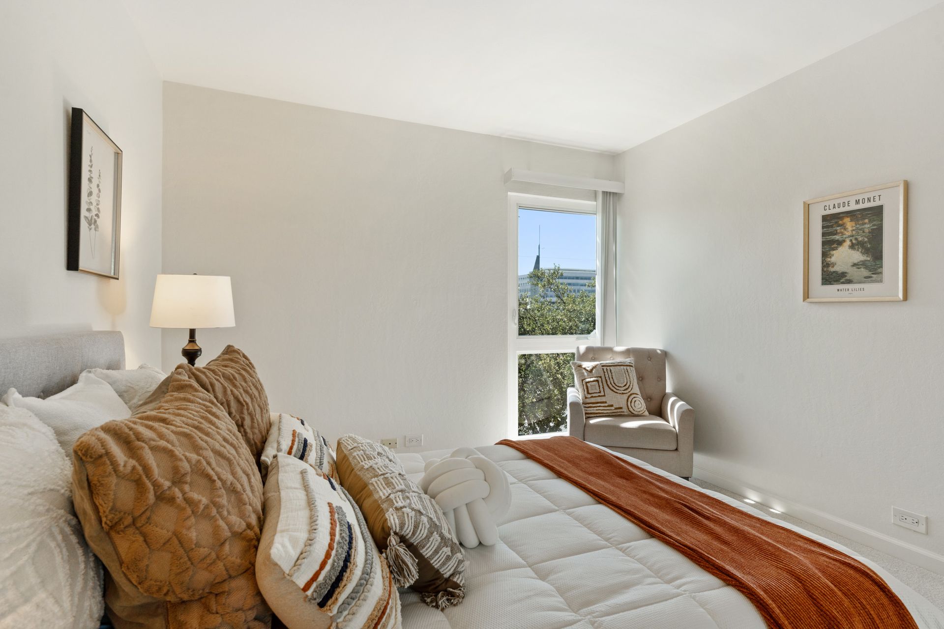 A bedroom with a bed , chair , lamp and window.