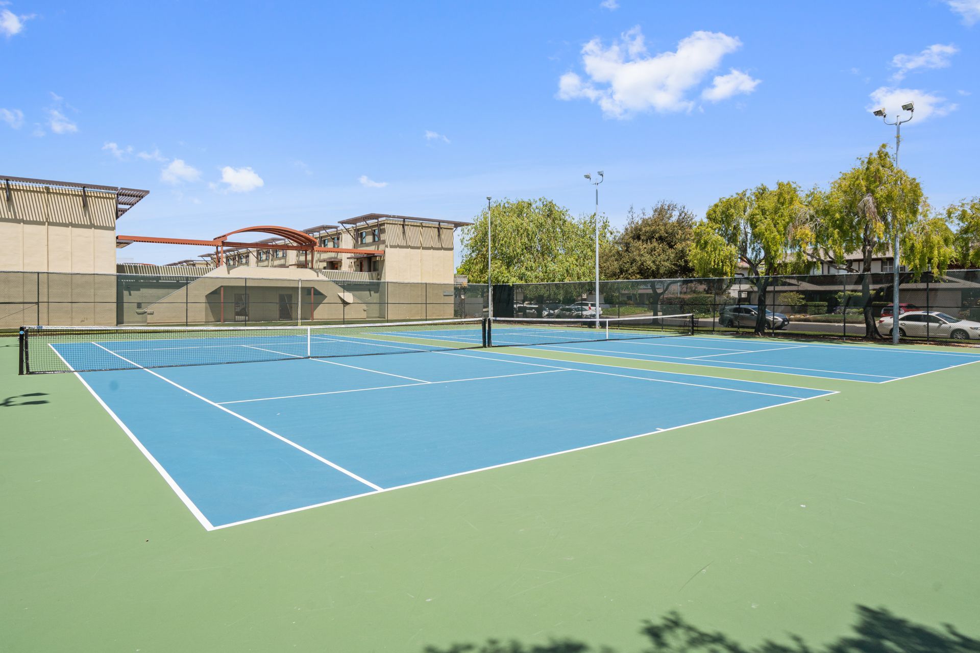 A tennis court with a building in the background and trees in the foreground.
