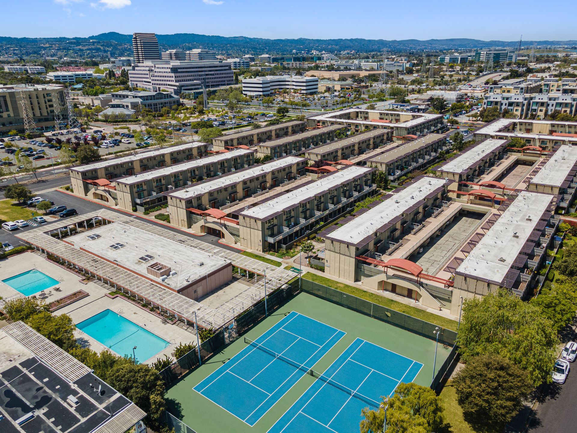 An aerial view of a tennis court surrounded by buildings and a swimming pool.