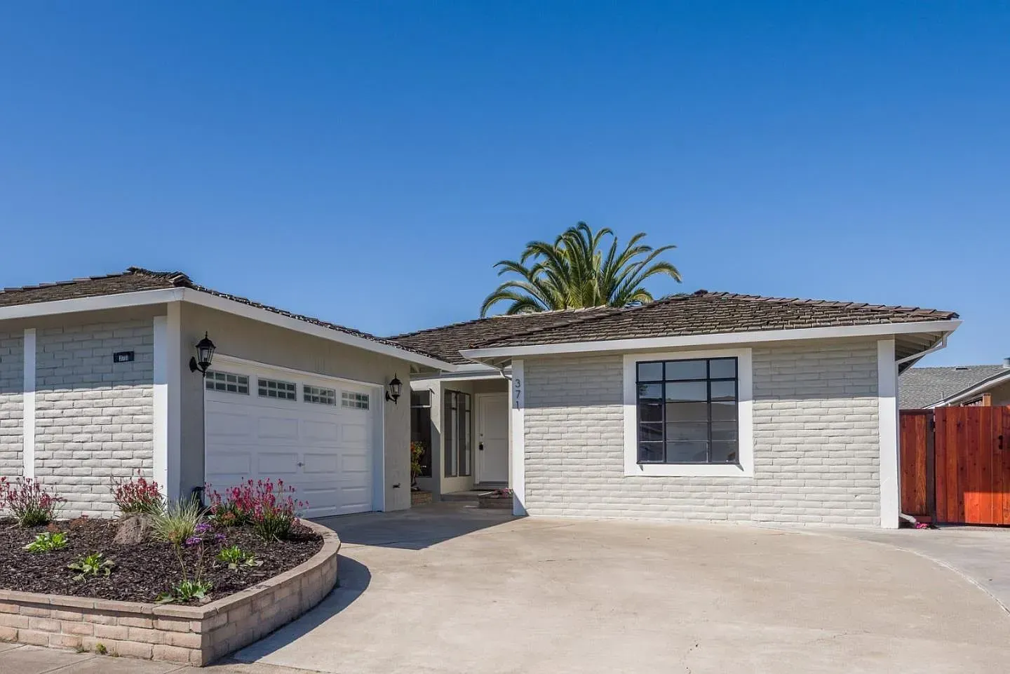 A white house with a garage and a palm tree in front of it.
