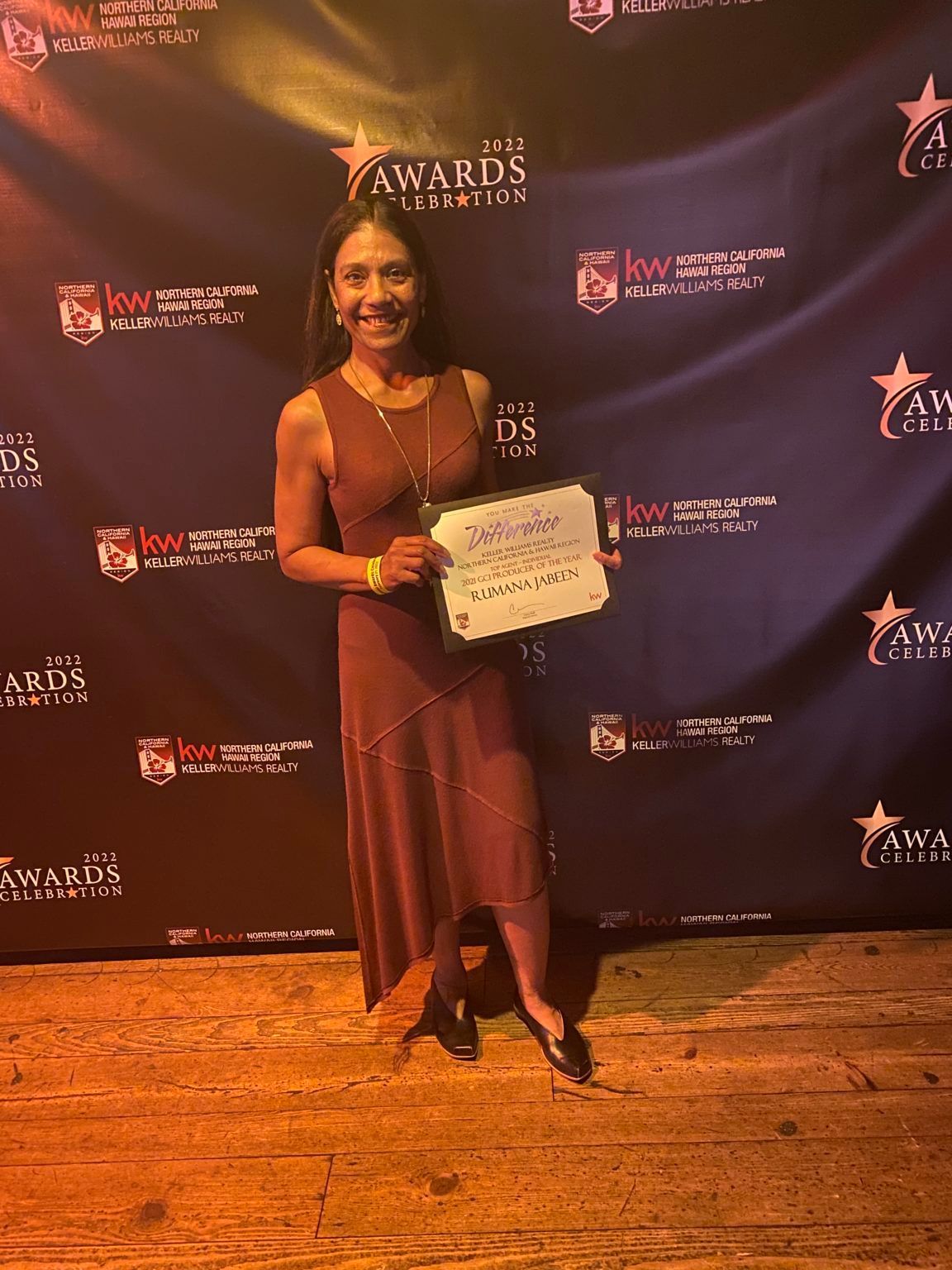 A woman in a red dress is standing in front of a blue backdrop holding a certificate.
