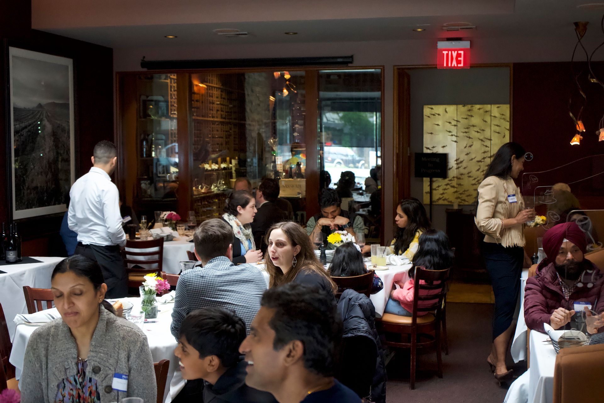 A group of people are sitting at tables in a restaurant with an exit sign above them