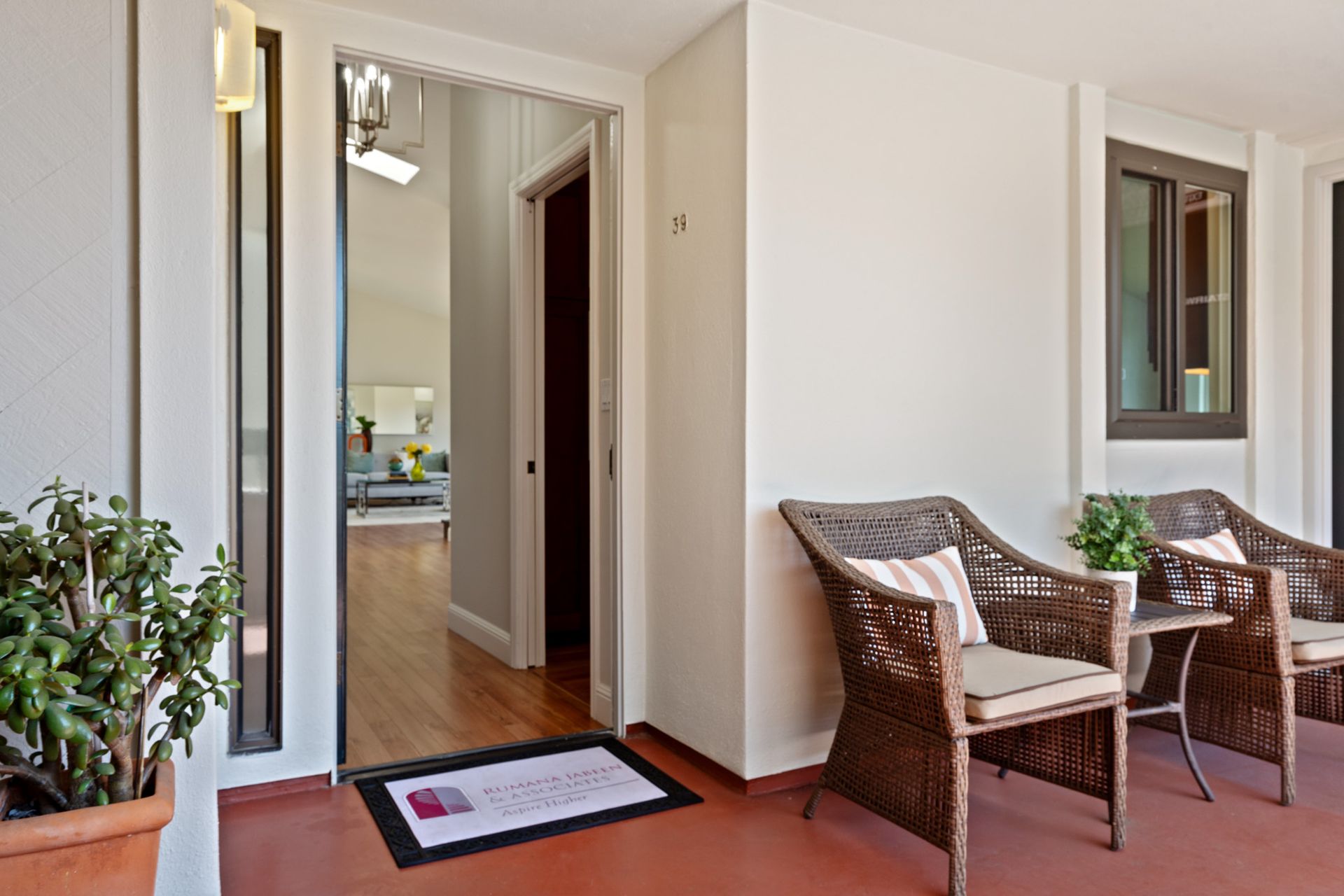 A porch with wicker chairs and a table with a welcome mat on it