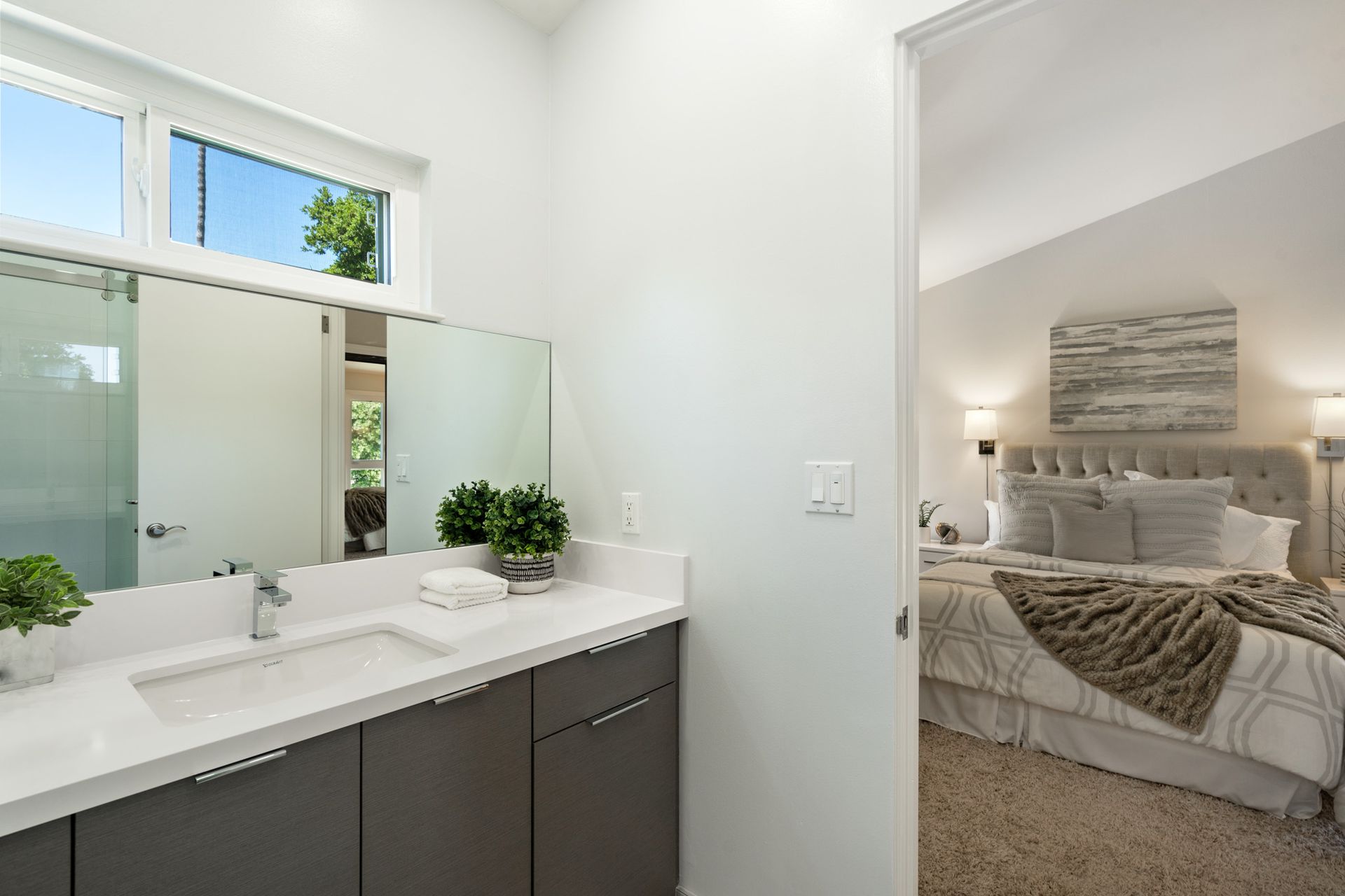 A bathroom with a double sink and a large mirror next to a bedroom.