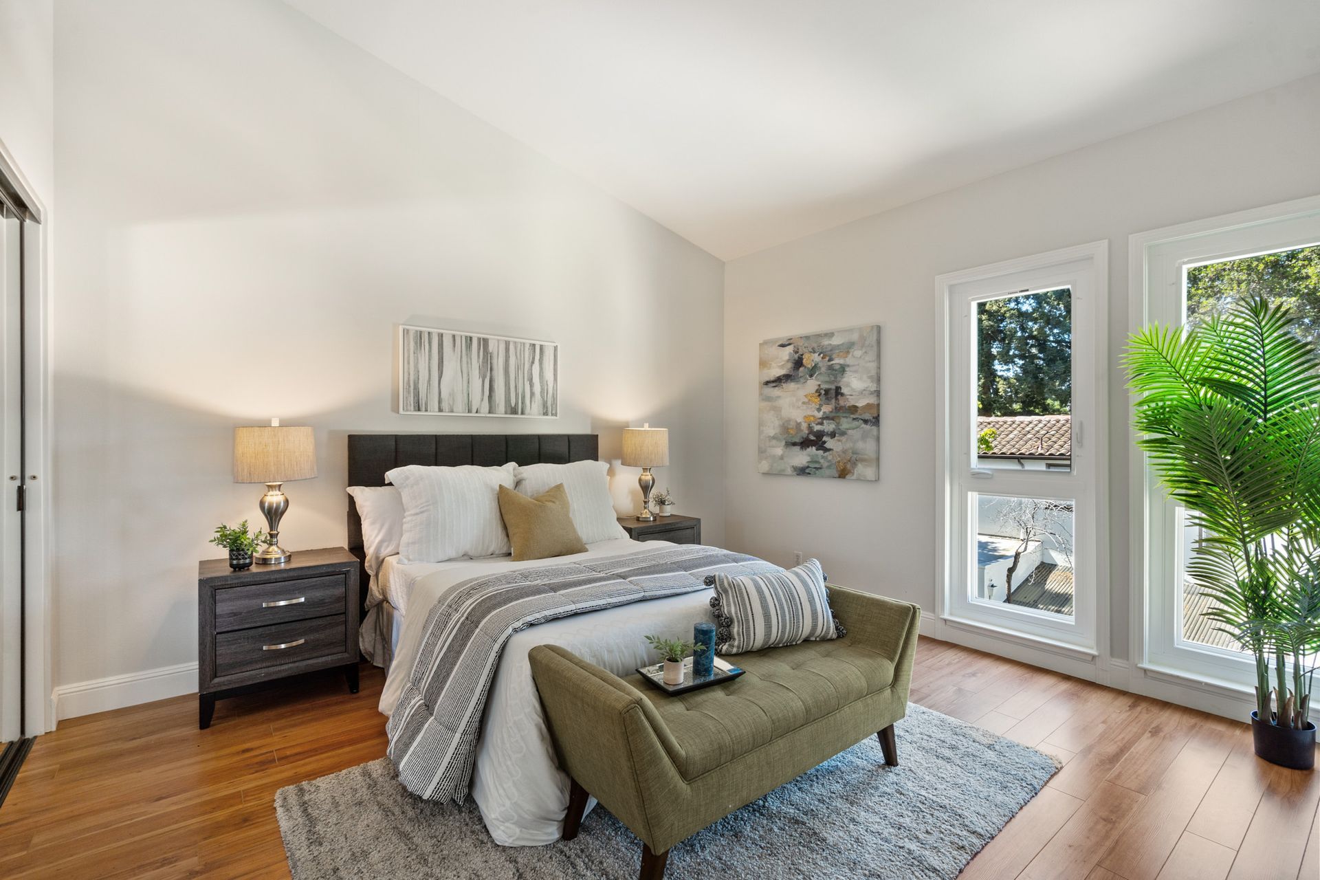 A bedroom with a bed , nightstand , bench and windows.