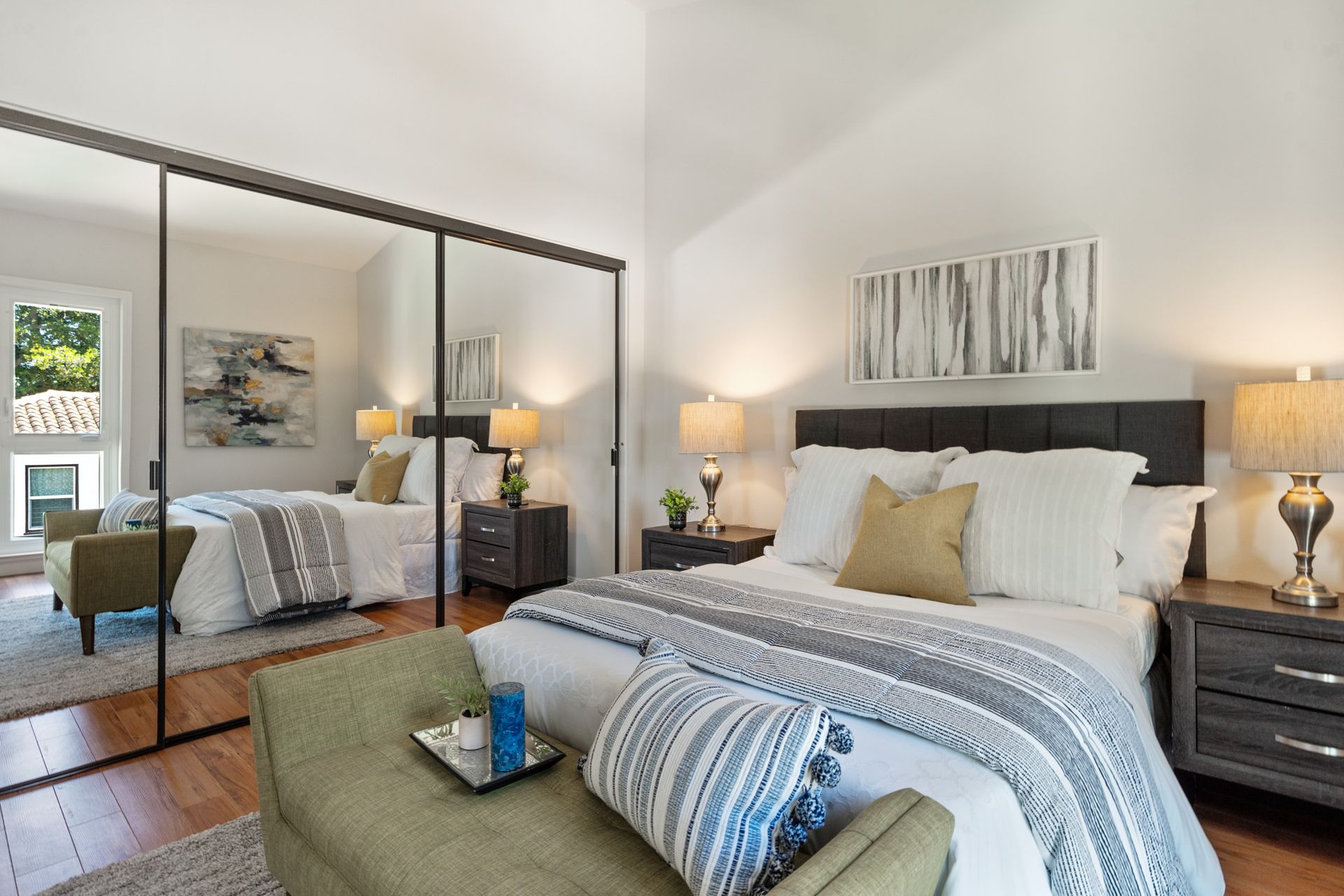 A bedroom with a large bed , sliding glass doors , nightstands , lamps and a bench.