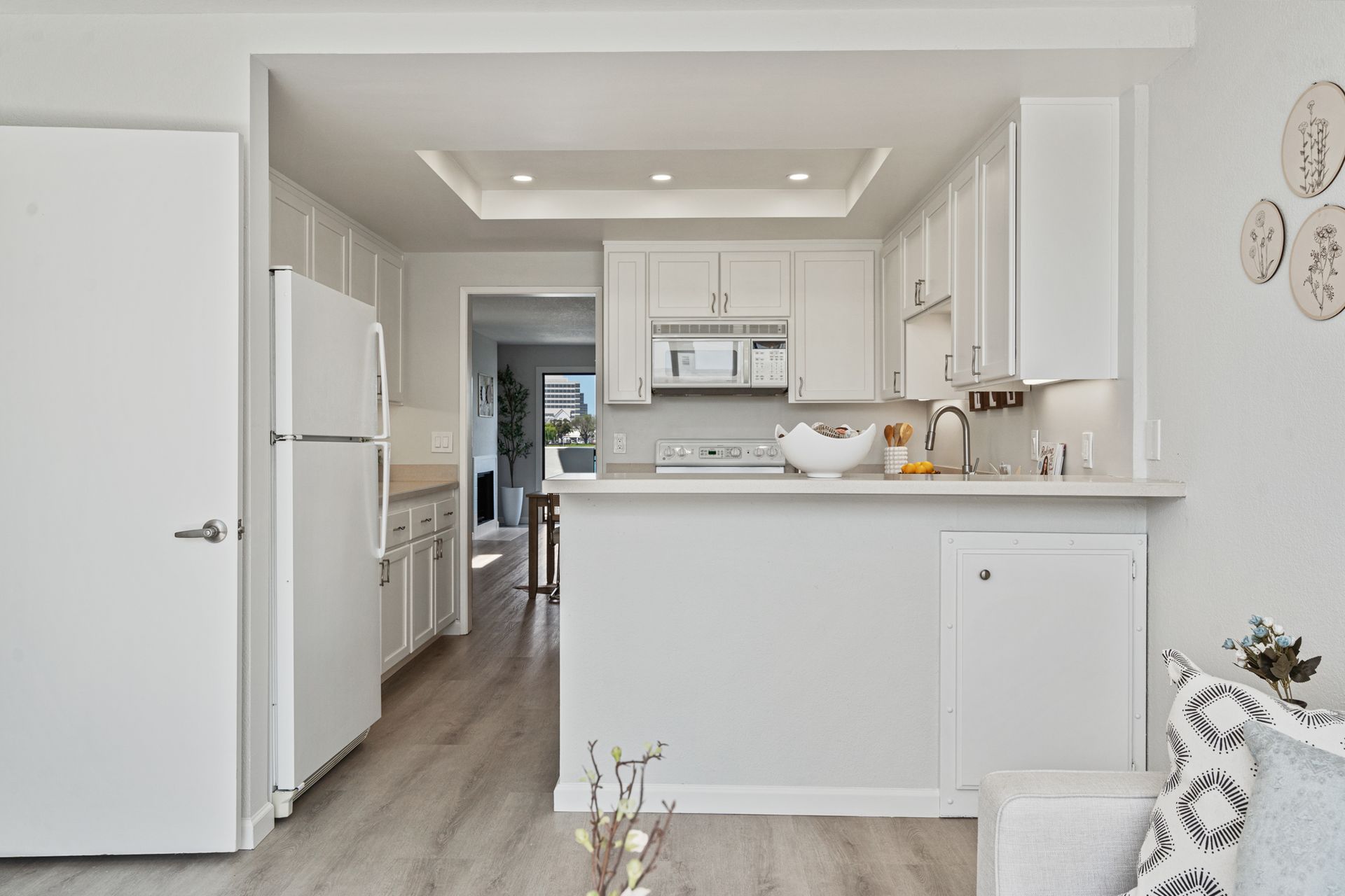 A kitchen with white cabinets , a refrigerator , a microwave and a sink.
