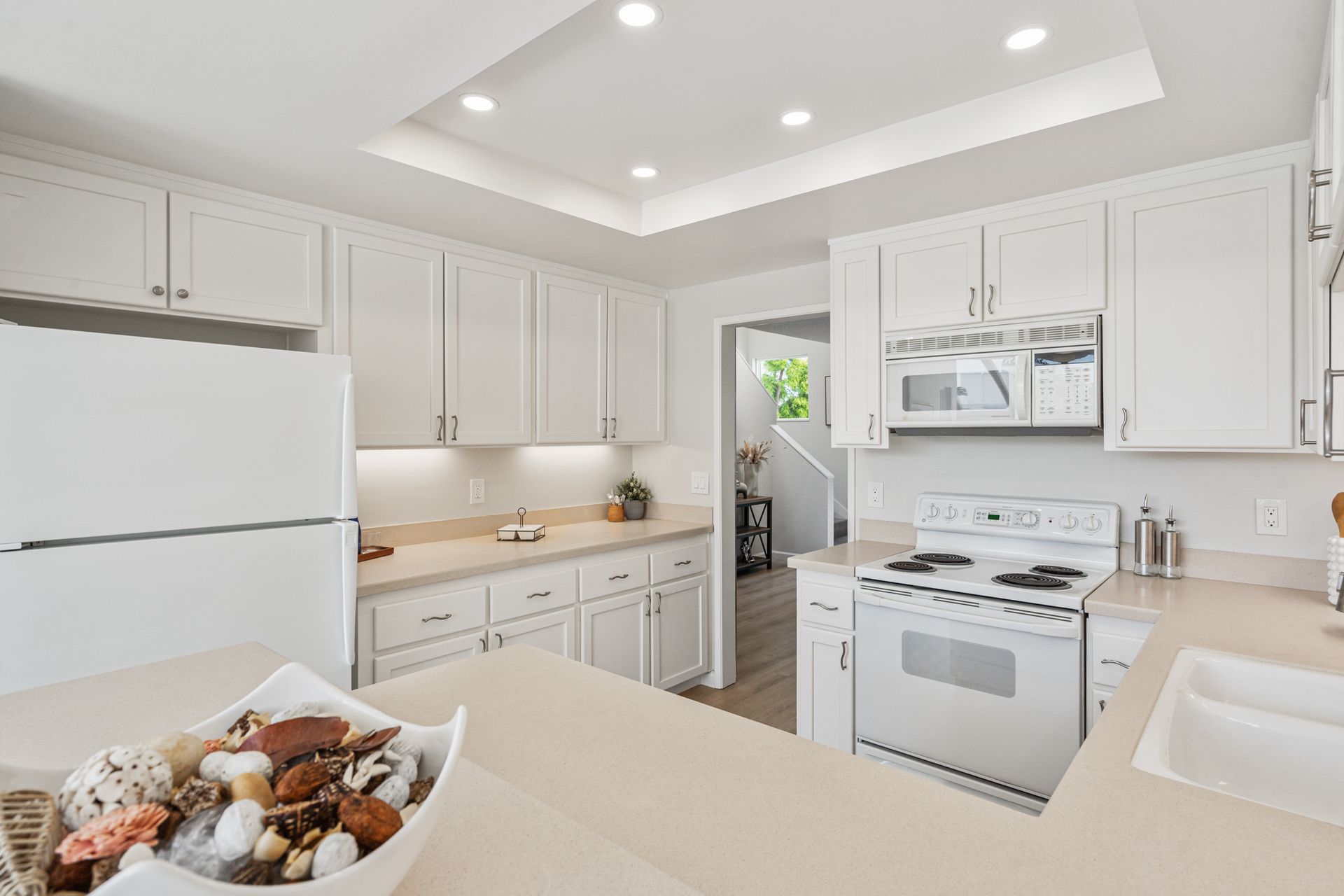 A kitchen with white cabinets , a stove , refrigerator , microwave and sink.