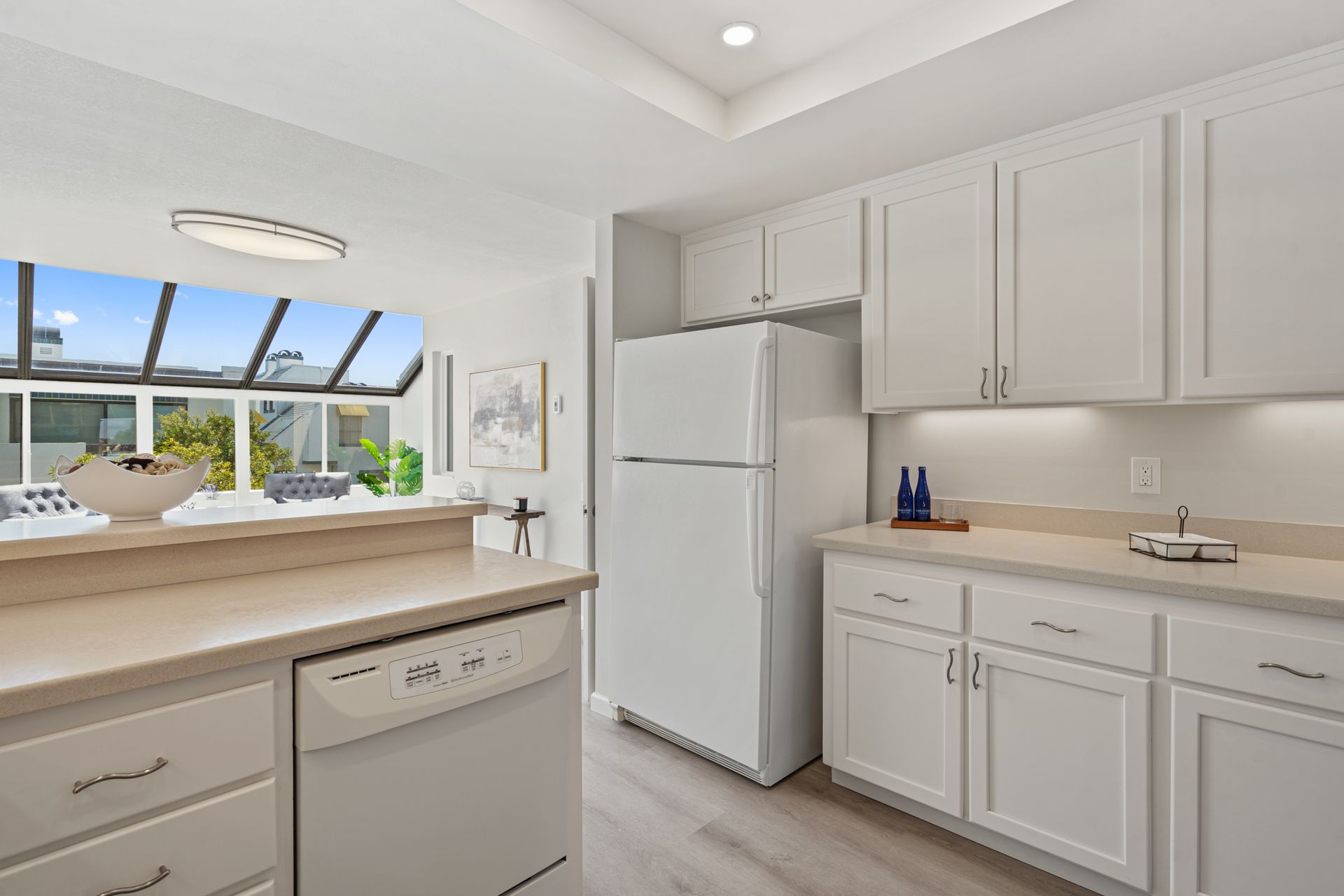 A kitchen with white cabinets , a refrigerator , a dishwasher , and a window.