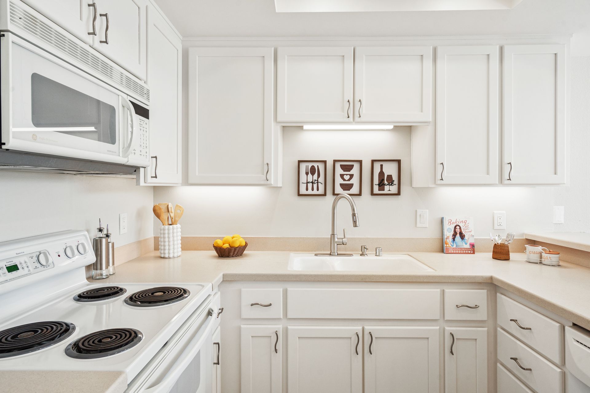 A kitchen with white cabinets , a stove , a sink , and a microwave.
