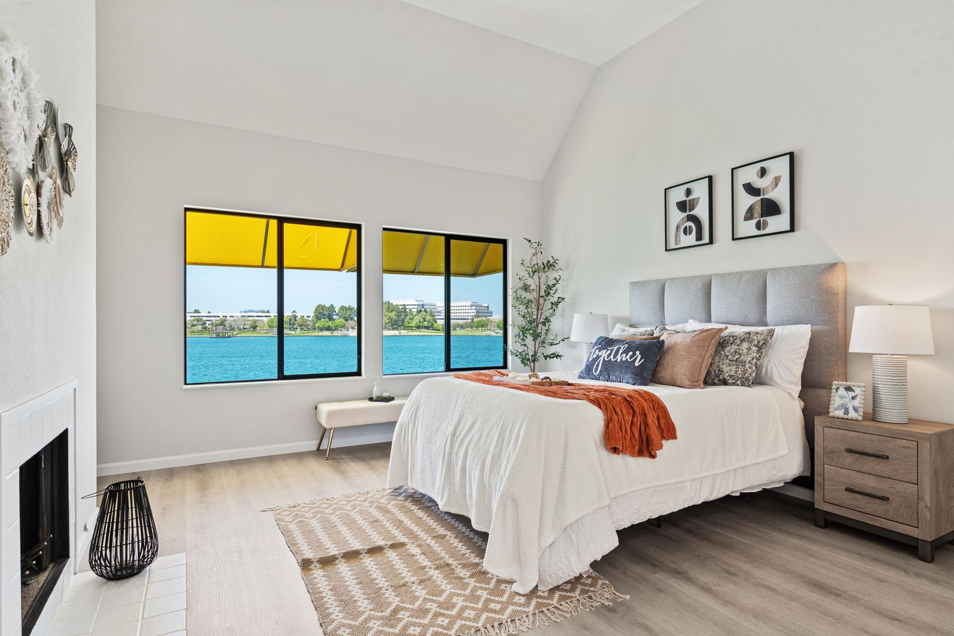 A bedroom with a bed , fireplace , and two windows overlooking a body of water.