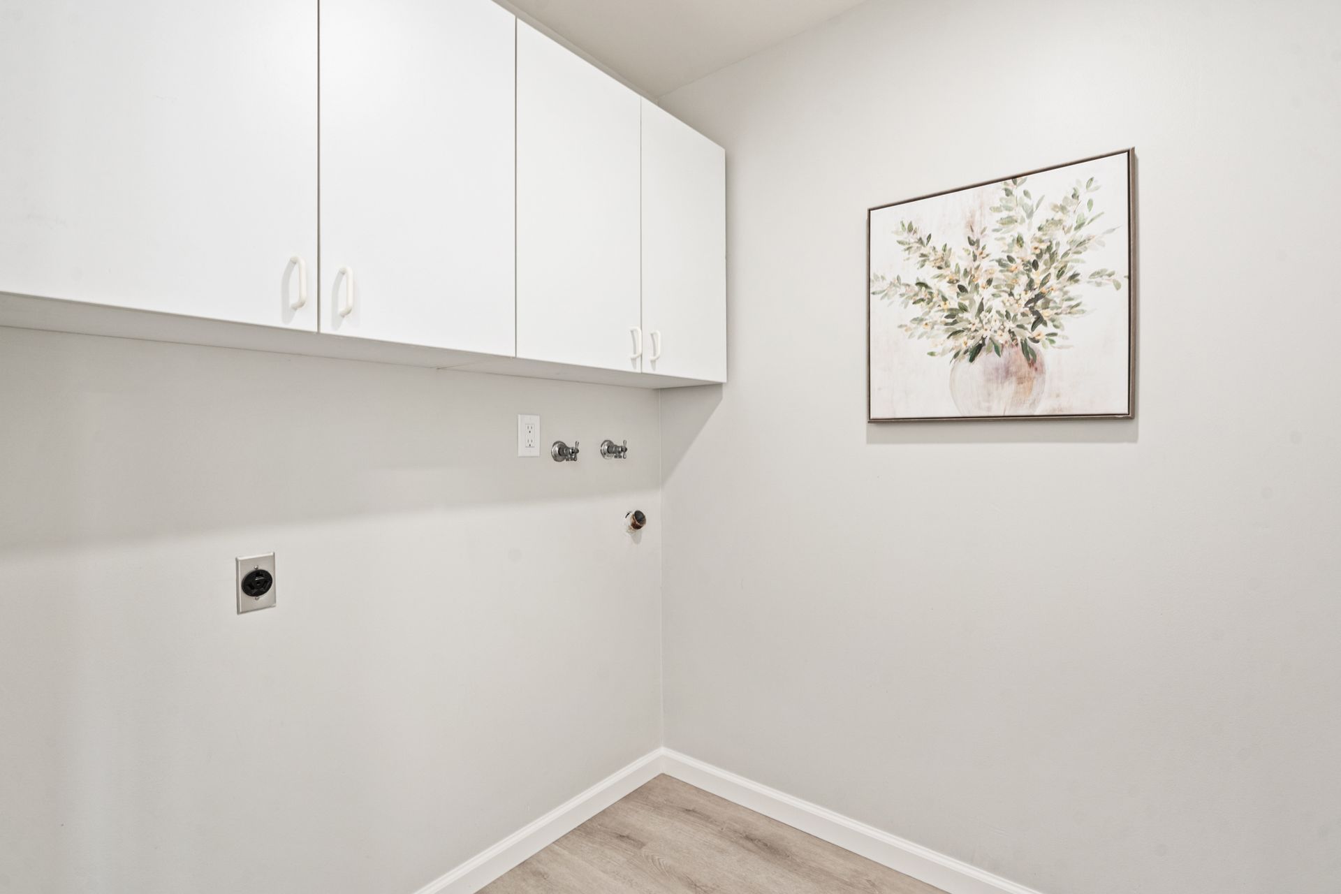 A laundry room with white cabinets and a painting on the wall.