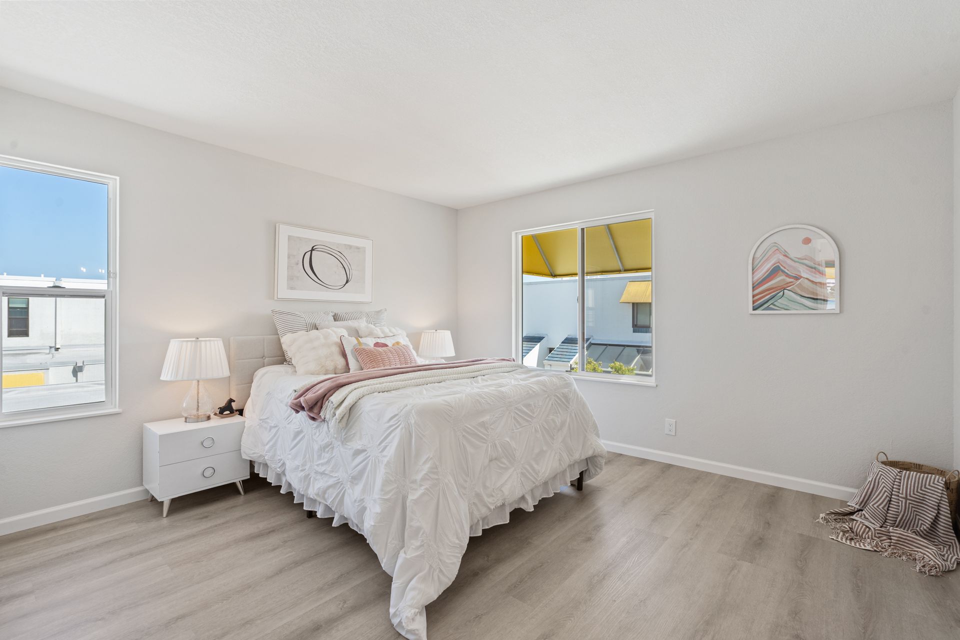 A bedroom with a bed , nightstand , and two windows.