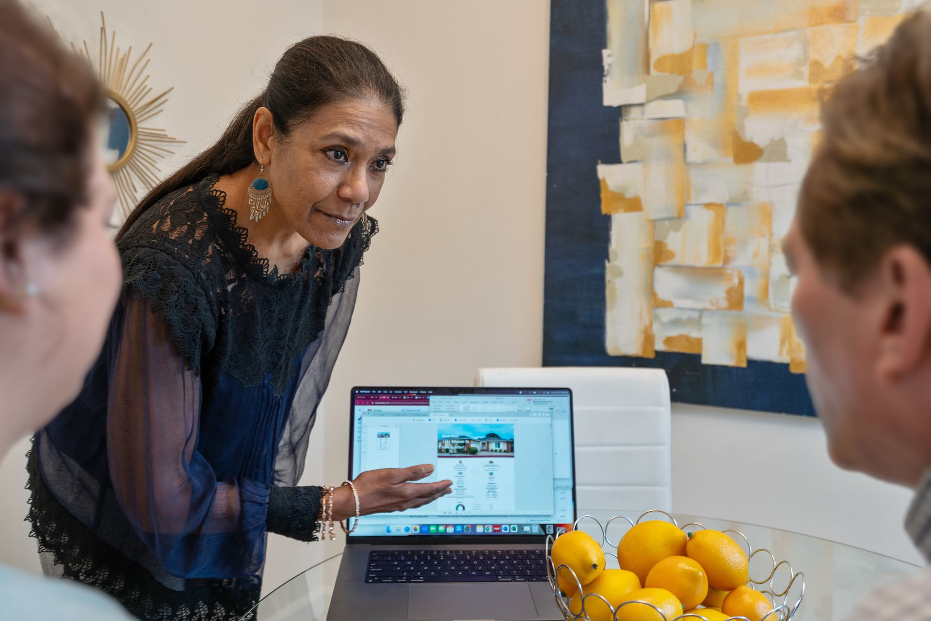 A woman is standing in front of a laptop computer talking to two people.