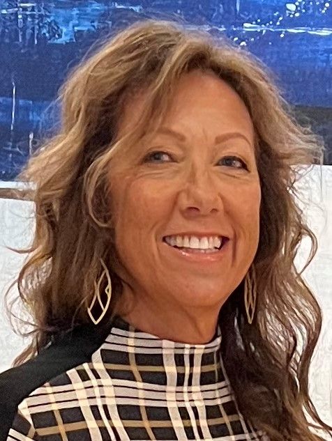 A woman in a plaid shirt is smiling in front of a painting.