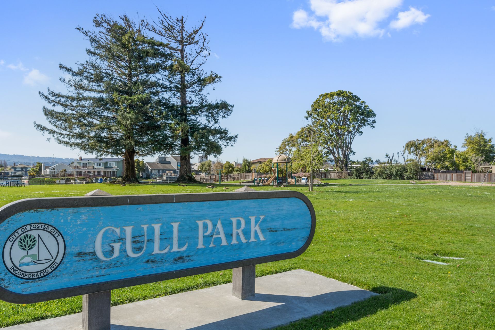 A blue sign that says gull park is in the middle of a grassy field.