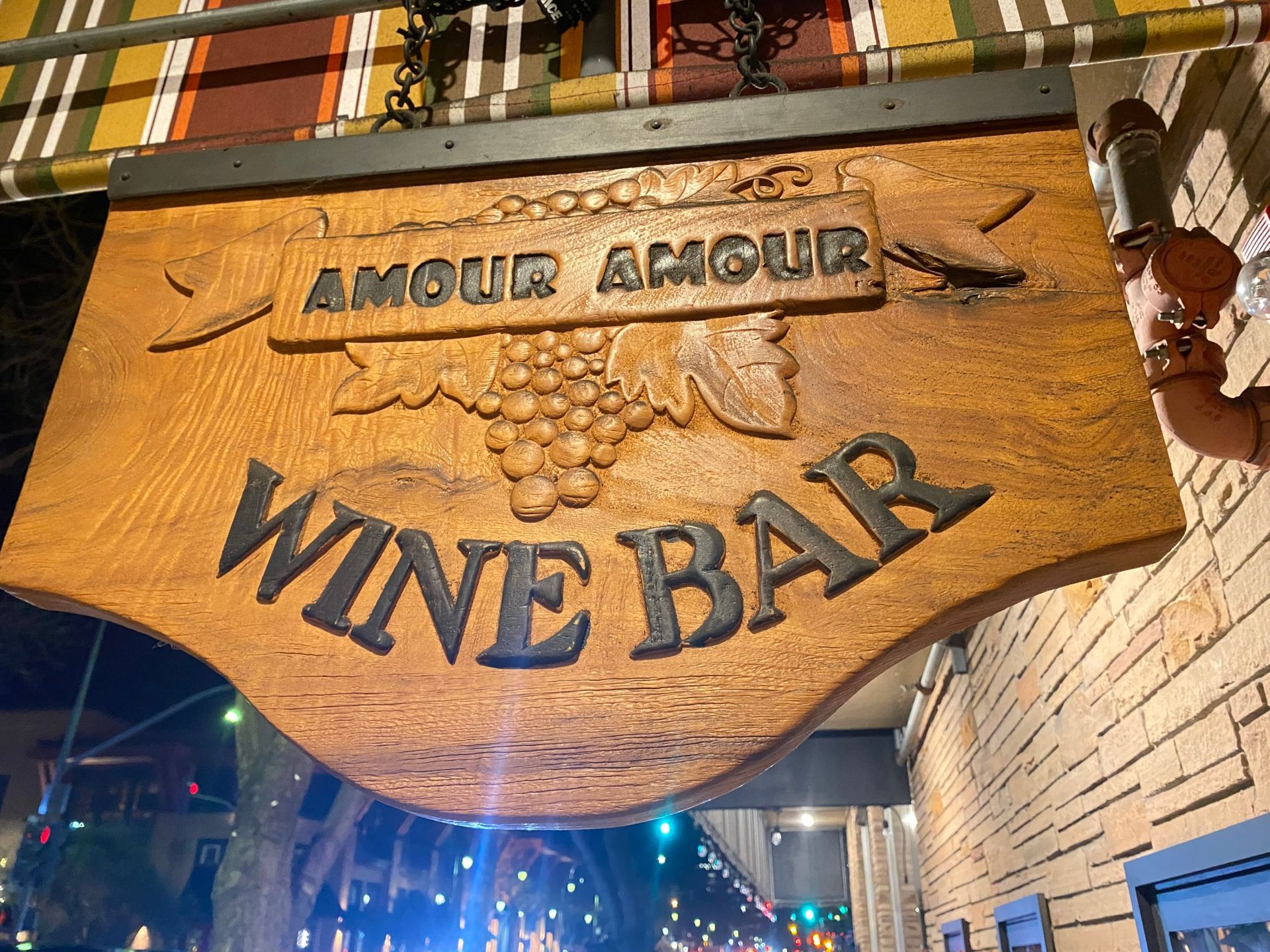 A wooden sign for amour amour wine bar hangs from a brick wall.