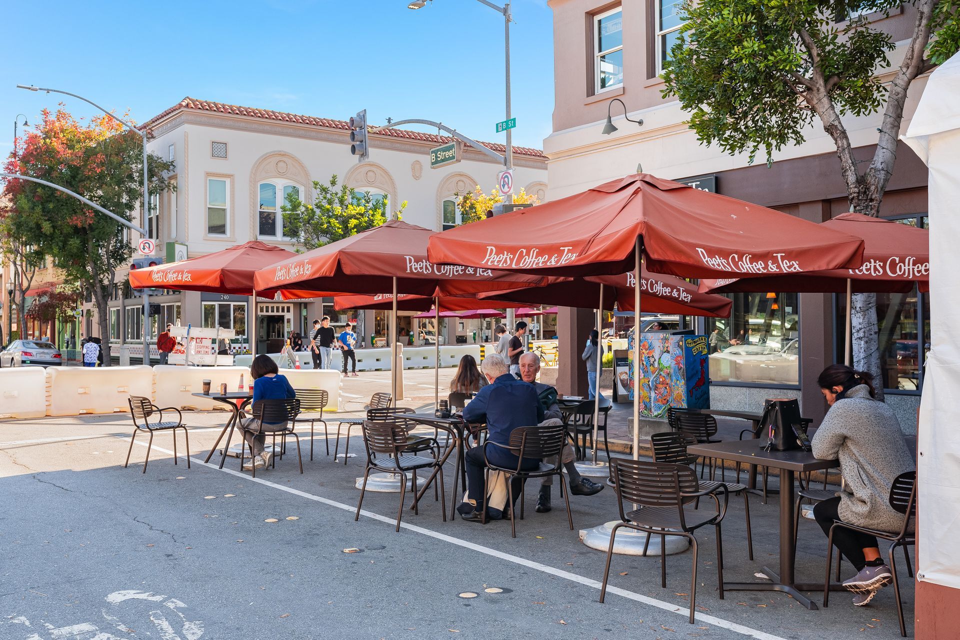 A group of people are sitting at tables under red umbrellas outside of a restaurant.