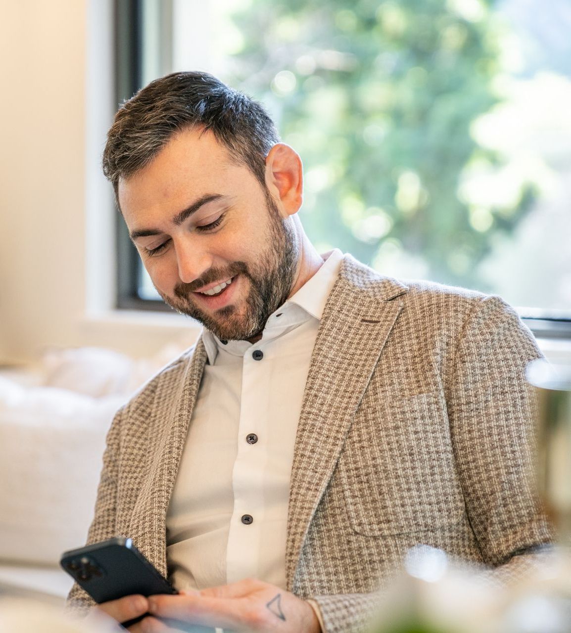 A man in a suit is smiling while looking at his phone
