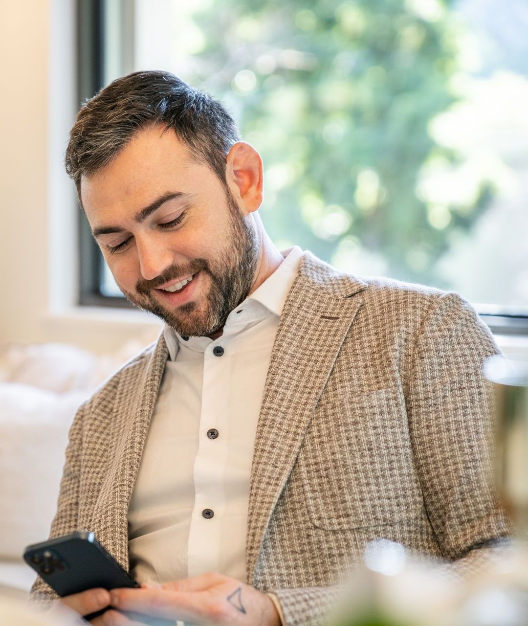 A man in a suit is smiling while looking at his cell phone.