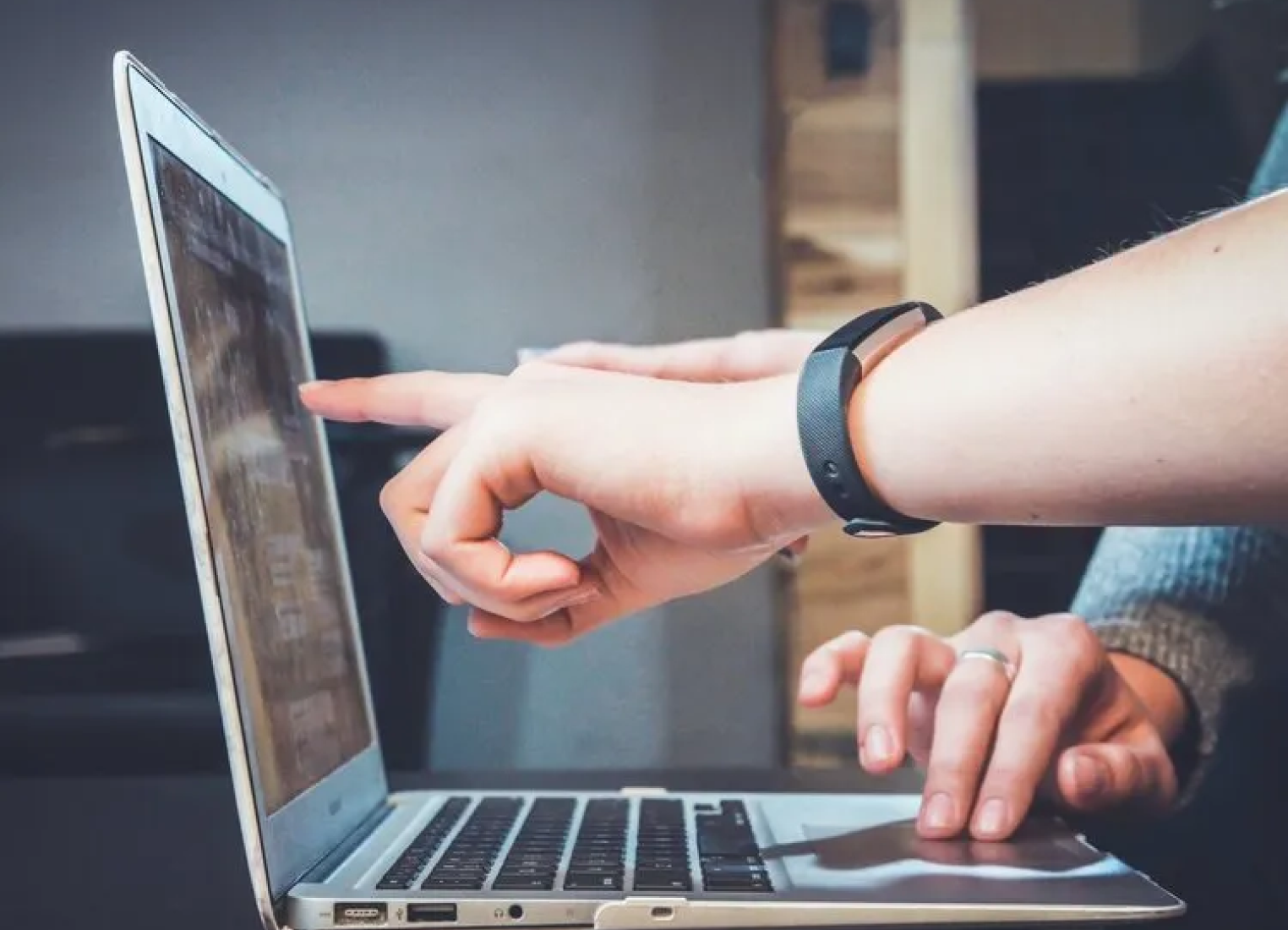 A person is using a laptop computer and pointing at the screen.