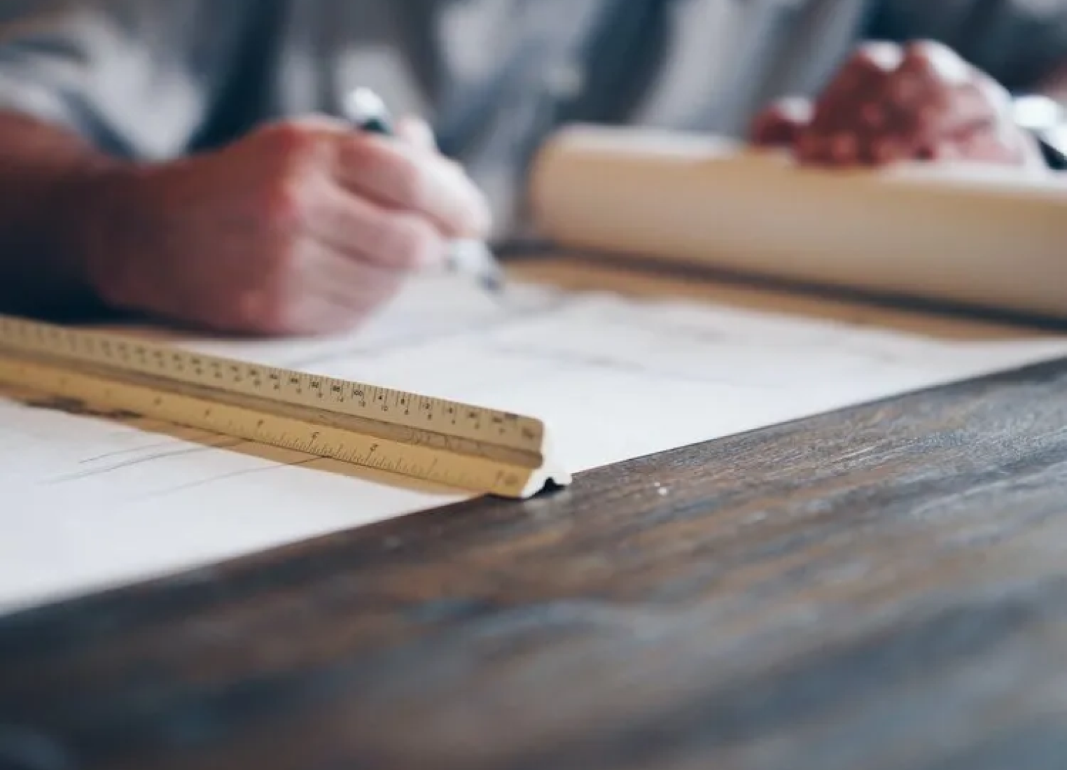 A person is sitting at a table with a ruler and a pen.