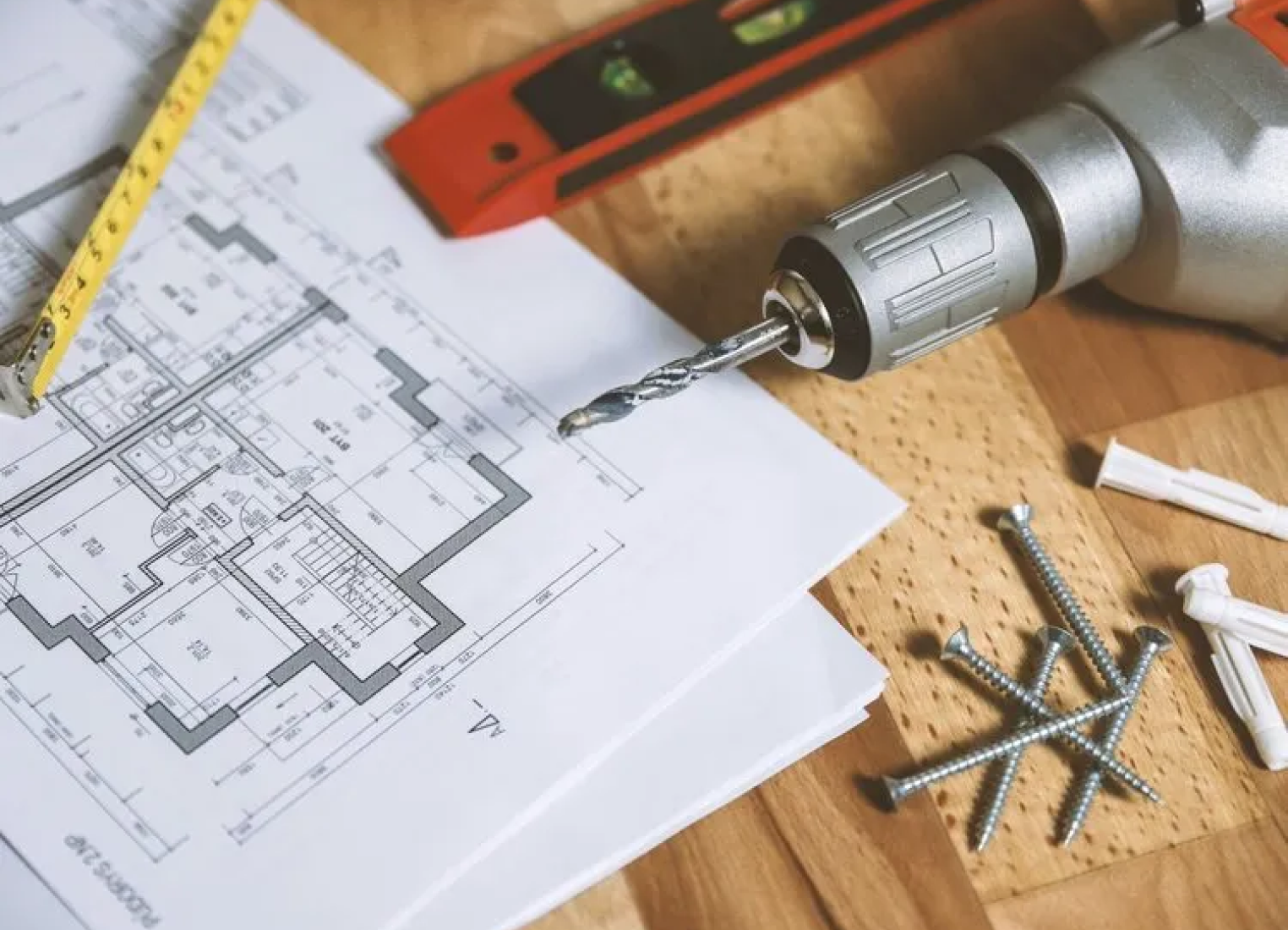 A drill is sitting on top of a house plan on a wooden table.