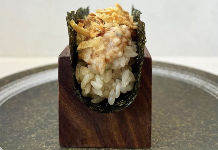 A close up of a sushi roll on a wooden block on a plate.