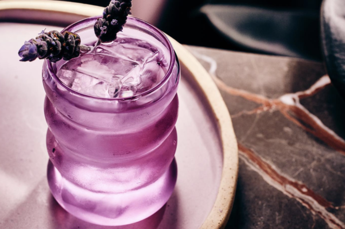 A purple drink with ice and lavender on a tray on a table.