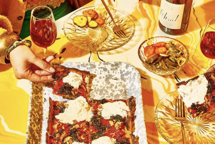 A person is taking a slice of pizza from a tray on a table.