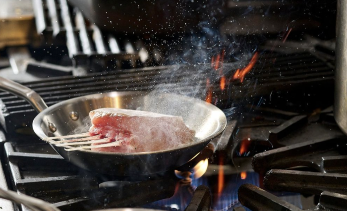 A piece of meat is being cooked in a frying pan on a stove.