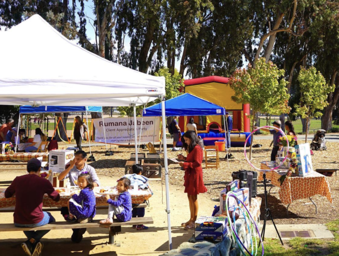A group of people are gathered under tents in a park