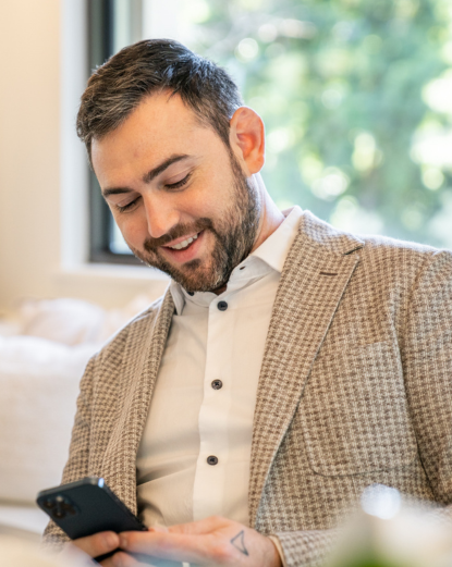 A man in a suit is smiling while looking at his cell phone.