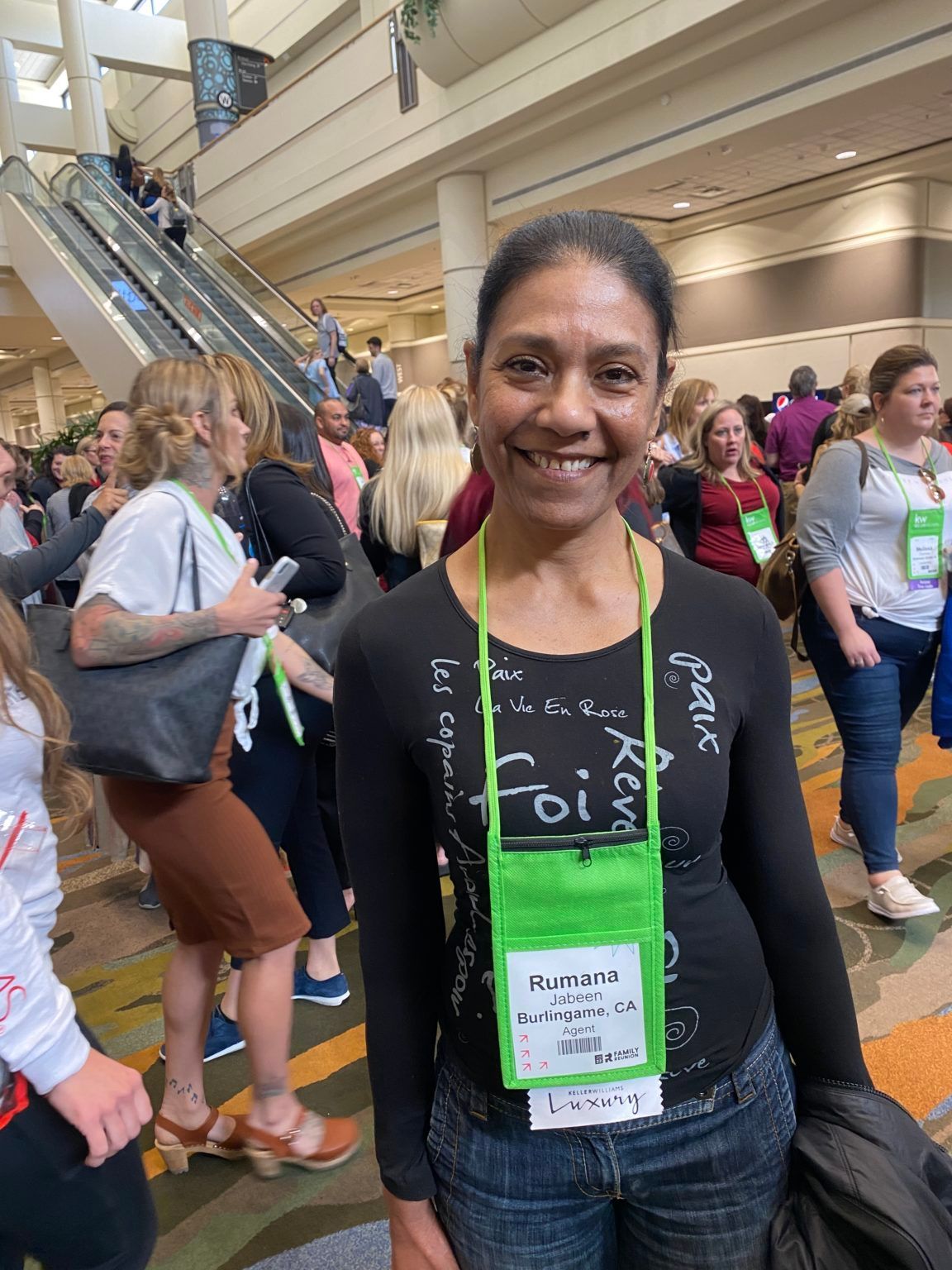 A woman wearing a name tag is smiling in front of a crowd of people.