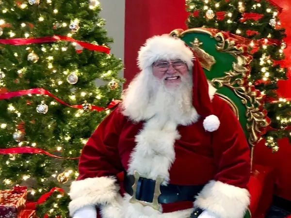 A man dressed as santa claus is sitting in front of a christmas tree