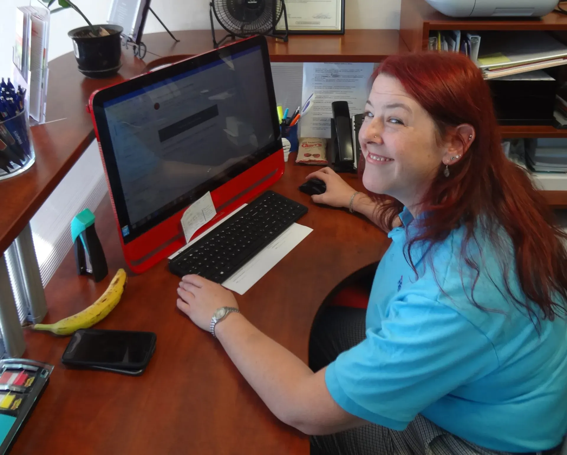 A woman in a blue shirt sits at a desk in front of a computer
