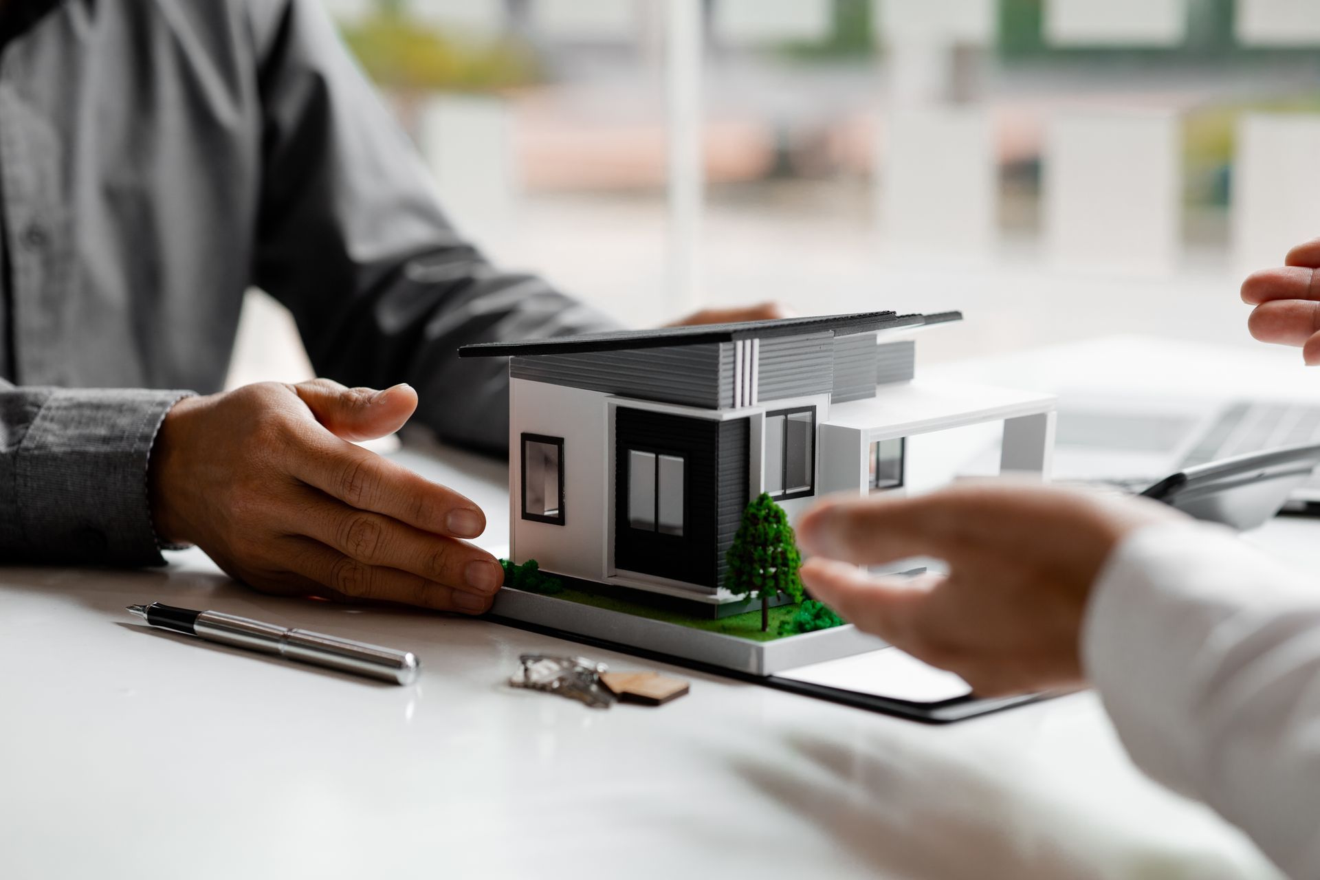 A man and a woman are sitting at a table with a model house and keys.