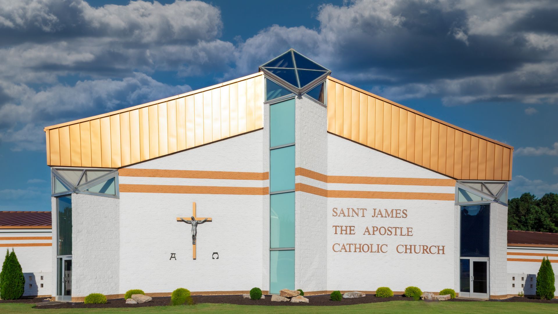 Church building with cross, sign, and grassy lawn. Copper roof and glass sections.