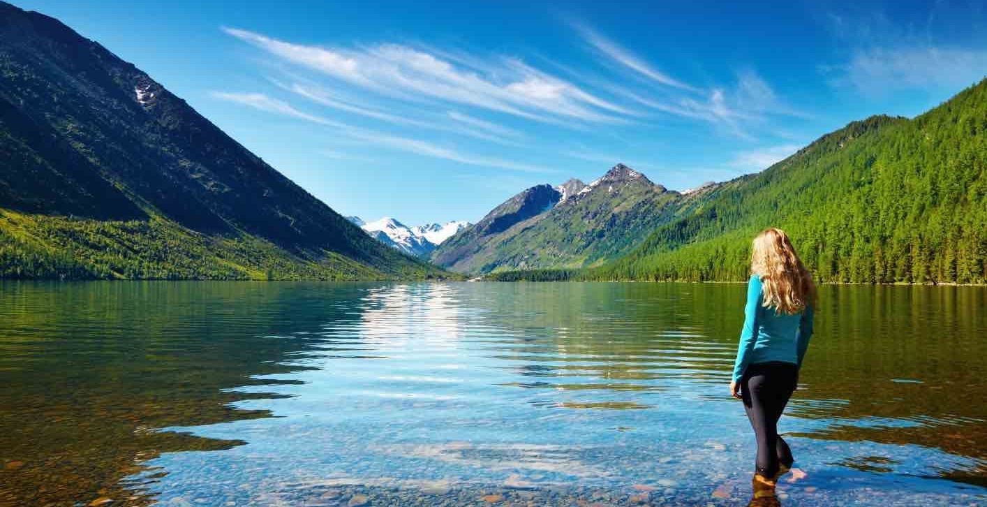 A woman standing in a lake looking at mountains and a beautiful blue sky