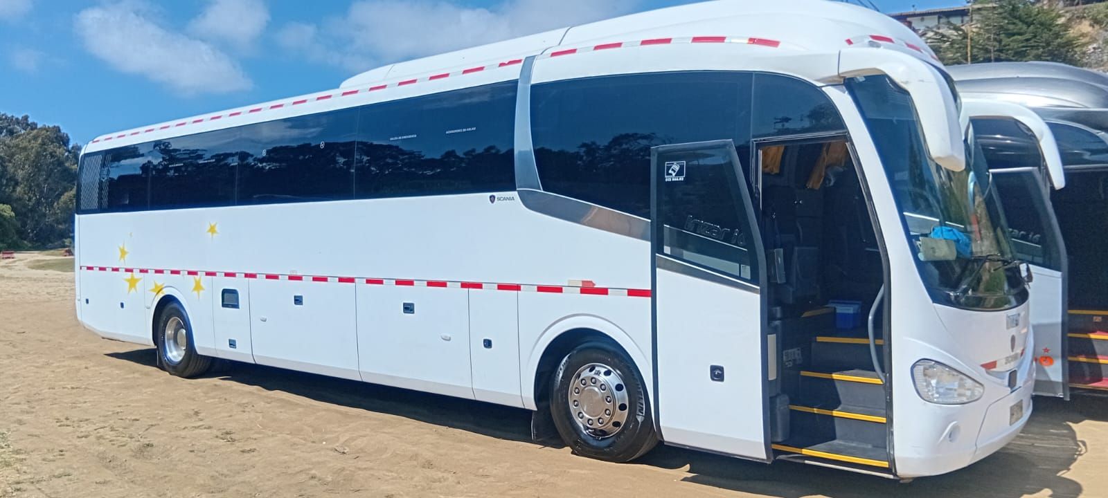 Un autobús blanco estacionado en un terreno de tierra con la puerta abierta, dejando ver unos escalones amarillos